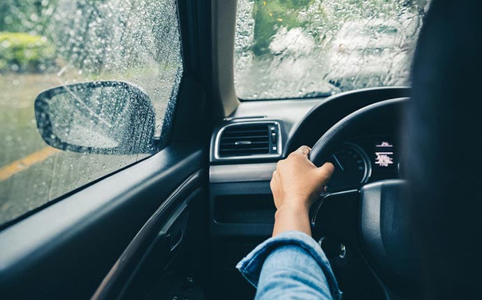 A closeup of a driver's hands on the steering wheel while driving in the rain